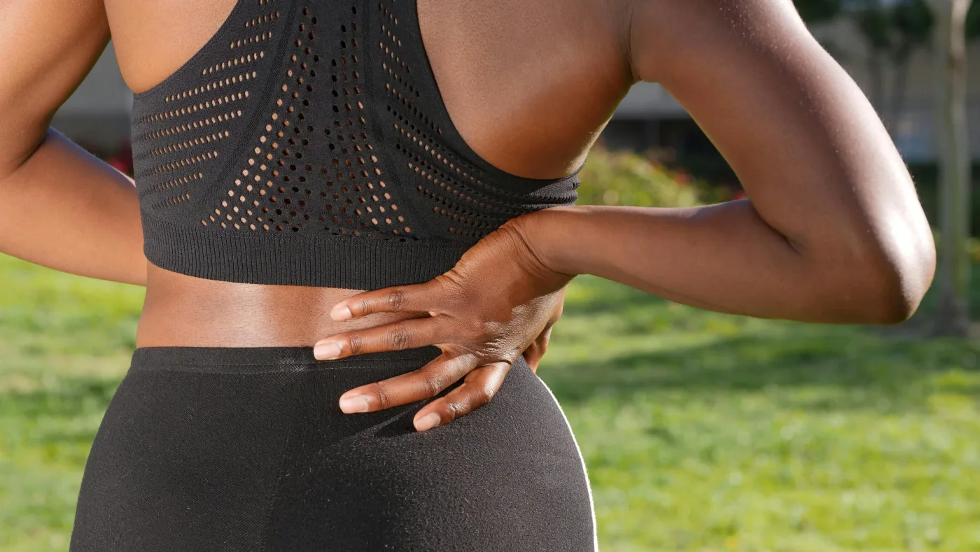 Woman wincing while holding her lower back at home
