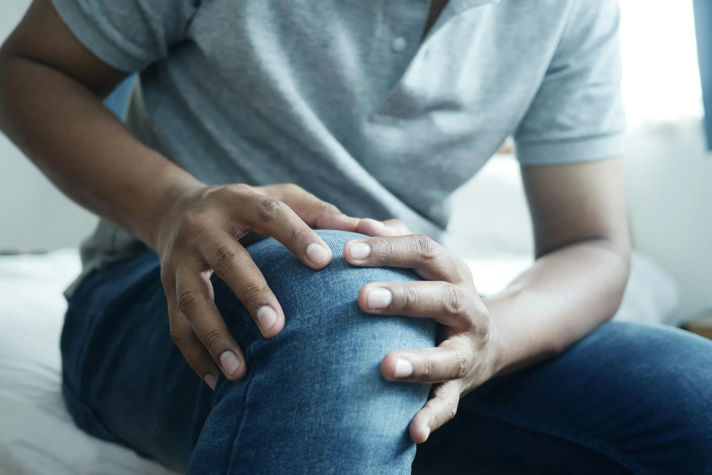 person clutching a painful knee while seated at home