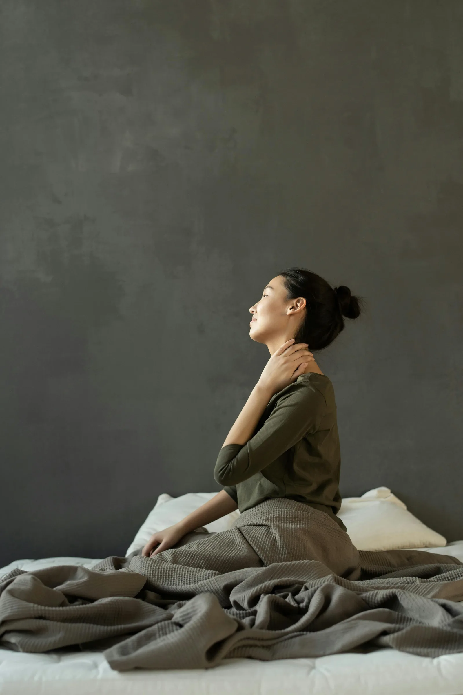 woman touching her neck in discomfort while sitting on a bed