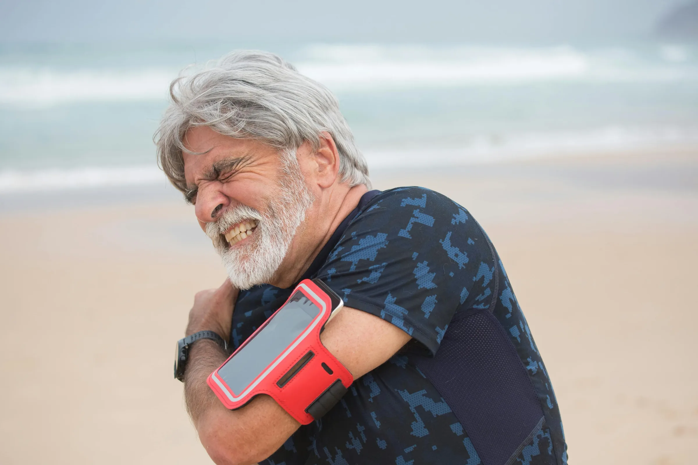 older man wincing while gripping his painful shoulder outdoors