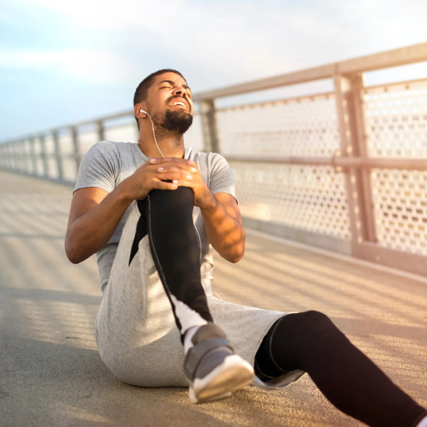 male runner wincing and holding his leg in pain during an outdoor run